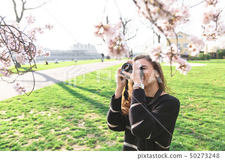 Girl makes photo of flowering tree in park outdoor 50273248