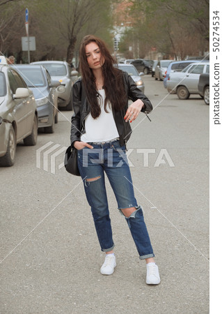 Sad woman in jeans posing with handbag in the center on the street 50274534