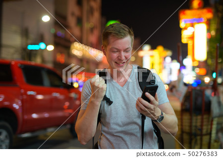 Happy tourist man backpacker using phone and getting good news in the busy street of Chinatown 50276383