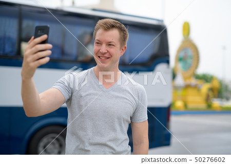 Young happy tourist man taking selfie against Ratchadamnoen street in Bangkok Young happy tourist man taking selfie against Ratchadamnoen street in Bangkok 50276602