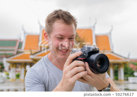 Face of happy tourist man photographing with camera against view of the Buddhist temple in Bangkok Face of happy tourist man photographing with camera against view of the Buddhist temple in Bangkok 50276617