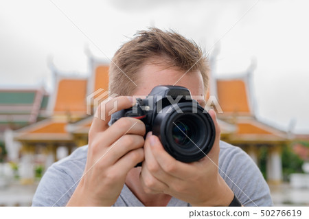 Tourist man photographing with camera against view of the Buddhist temple in Bangkok Tourist man photographing with camera against view of the Buddhist temple in Bangkok 50276619