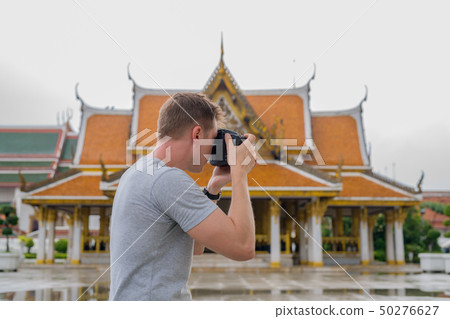 Profile view of young tourist man taking picture with camera of the Buddhist temple in Bangkok Profile view of young tourist man taking picture with camera of the Buddhist temple in Bangkok 50276627