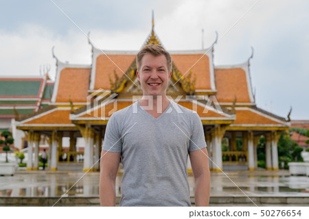 Young happy tourist man smiling against view of the Buddhist temple in Bangkok 50276654
