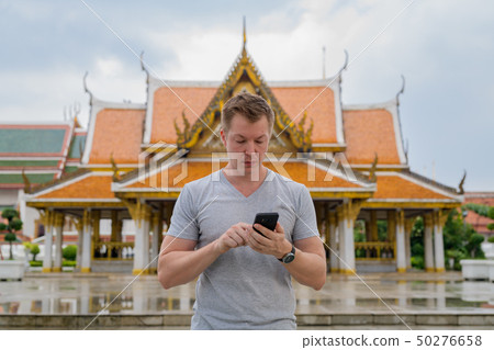 Young tourist man using phone against view of the Buddhist temple in Bangkok Young tourist man using phone against view of the Buddhist temple in Bangkok 50276658