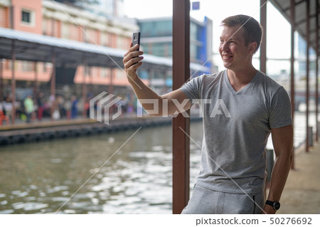 Young happy tourist man taking selfie at the local pier in Bangkok Young happy tourist man taking selfie at the local pier in Bangkok 50276692