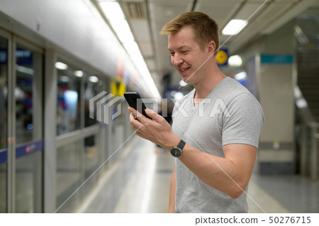 Young happy tourist man using phone at the underground train station in Bangkok Young happy tourist man using phone at the underground train station in Bangkok 50276715