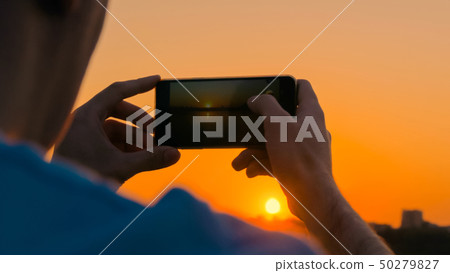 Man taking photo of sunset with smartphone on city quay 50279827