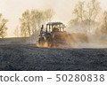 Sowing time. Blue tractor rides through the agricultural field in the sunlight. 50280838