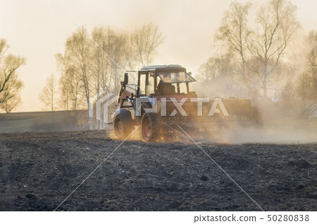 Sowing time. Blue tractor rides through the agricultural field in the sunlight. 50280838