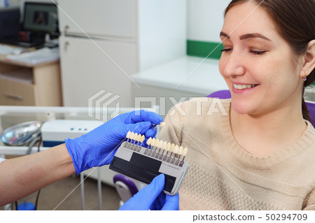 Dentist with tooth color samples is choosing shade for women patient teeth at dental clinic. Dentist with tooth color samples is choosing shade for women patient teeth at dental clinic. 50294709