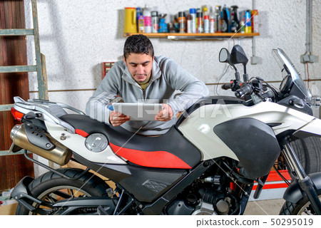 young man using a tablet next to motorcycle 50295019