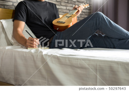 Happy young asian man playing ukulele sitting on Happy young asian man playing ukulele sitting on 50297643