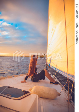 girl with long hair sitting at the stern of the yacht and looks into the distance at sunset 50305941