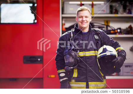 Photo of happy male firefighter with helmet in his hands against background of fire truck 50310596
