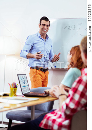 Positive cheerful young man smiling to students Positive cheerful young man smiling to students 50323376