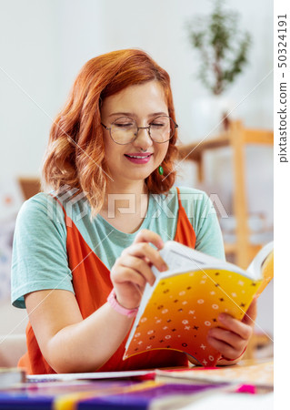 Pleasant young woman looking into her copybook Pleasant young woman looking into her copybook 50324191