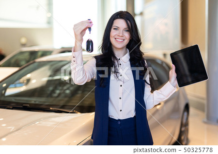 Happy woman buyer possing with keys near her new vehicle in car dealership 50325778