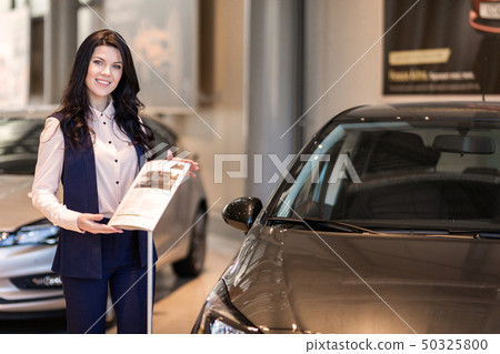 Beautiful saleswoman possing near new car in dealership center Beautiful saleswoman possing near new car in dealership center 50325800