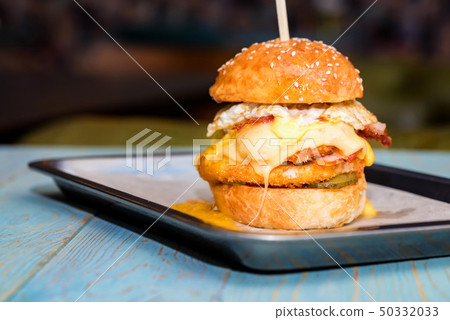 Close up tall tasty burger with cheese and egg served on tray 50332033