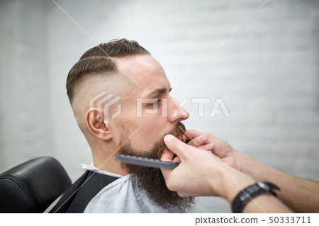 Brutal guy in modern Barber Shop. Hairdresser makes hairstyle a man with a long beard. Master 50333711