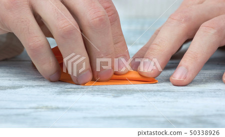 Close up male hands folding orange paper. 50338926