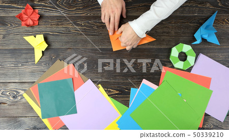 Hands of guy make origami crane with orange paper. Hands of guy make origami crane with orange paper. 50339210
