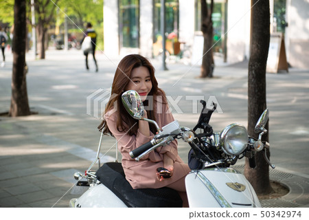 Young woman sitting on a motorbike and making-up Young woman sitting on a motorbike and making-up 50342974