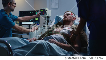 Injured soldier lying in hospital among doctor and nurse 50344767