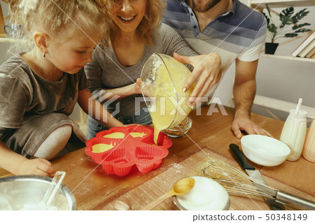 Cute little girl and her beautiful parents preparing the dough for the cake in kitchen at home Cute little girl and her beautiful parents preparing the dough for the cake in kitchen at home 50348149