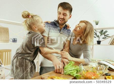 Cute little girl and her beautiful parents are cutting vegetables in kitchen at home 50349329