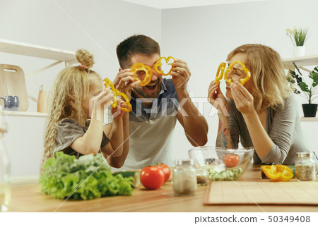 Cute little girl and her beautiful parents are cutting vegetables in kitchen at home 50349408