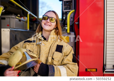 Photo of smiling fire woman in glasses with helmet in hands sitting in fire truck 50350252