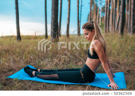 Girl in sportswear leggings and top. In the summer on a rug in forest, park. Tanned skin is a Girl in sportswear leggings and top. In the summer on a rug in forest, park. Tanned skin is a 50362509