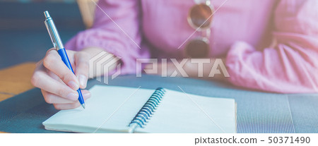 Woman hand is writing on a notepad with a pen. Woman hand is writing on a notepad with a pen. 50371490