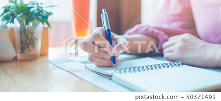 Woman hand is writing on a notepad with a pen. 50371491