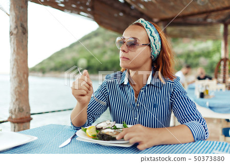 Young woman eating oyster in an outdoor restaurant Young woman eating oyster in an outdoor restaurant 50373880