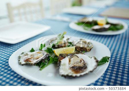 Fresh oysters on a white plate with green salad and lemon on a blue tablecloth 50373884