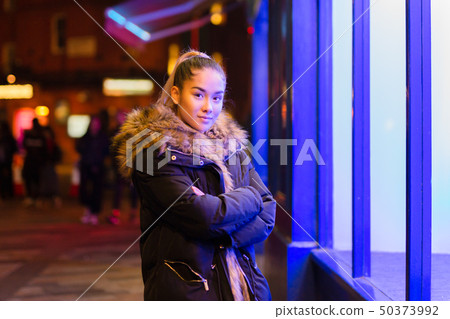 Mixed race teenage with fur coat standing next to window with blue light 50373992