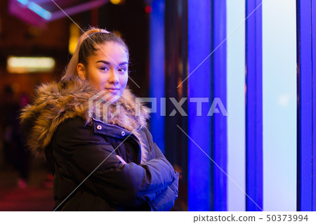 Mixed race teenage with fur coat standing next to window with blue light. 50373994