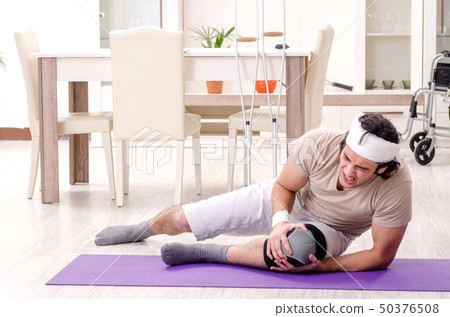 Injured young man doing exercises at home  50376508