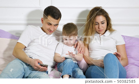 Family with child are looking in their mobile phones laying on the bed. Dependence from gadgets. Family with child are looking in their mobile phones laying on the bed. Dependence from gadgets. 50382585