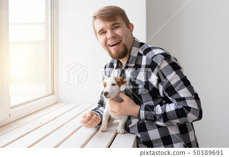 people, pets and animals concept - young man hugging puppy near window on white background 50389691