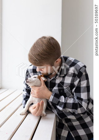 people, pets and animals concept - young man hugging jack russell terrier puppy near window on white 50389697
