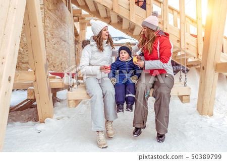 A young seed mother, a little son and girlfriend in winter in the city, ride on a wooden swing. Rest A young seed mother, a little son and girlfriend in winter in the city, ride on a wooden swing. Rest 50389799