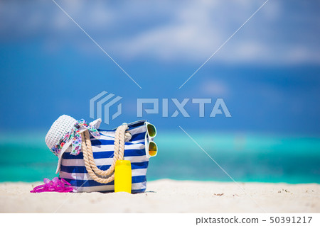 Blue bag, straw white hat, sunglasses, flip flop and sunscreen bottle on tropical beach 50391217