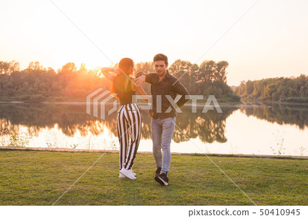 Romantic, social dance, people concept - young couple dancing bachata near the lake in sunny day Romantic, social dance, people concept - young couple dancing bachata near the lake in sunny day 50410945