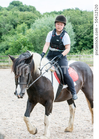 A girl practicing riding on a black and white horse 50412520