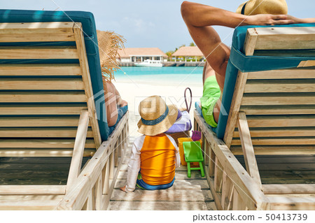 Family at beach on wooden sun bed loungers 50413739