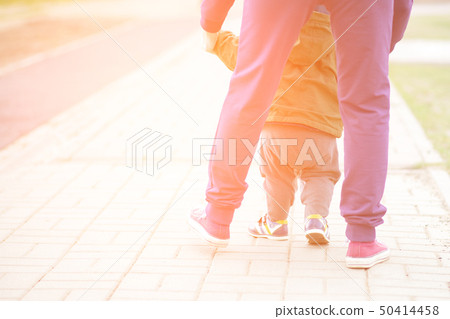 Cute baby boy learning to walk and make his first steps. mom is holding his hand. child's feet close Cute baby boy learning to walk and make his first steps. mom is holding his hand. child's feet close 50414458
